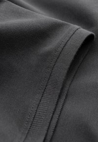 Close-up van een zwart T-shirt met korte mouwen waarop de gestructureerde stof en een keurig gestikte zoom te zien zijn. Geen zichtbare logo’s, patronen of accessoires.