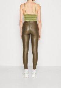 Olivgrön, högmidjade imitationläderleggings med bakfickor, figurnära design och slät textur; bärs med en randig linne och sneakers.