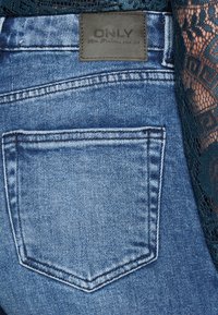 Modré džíny z denimu s kapesní na zádech, které mají vyšitou dekoraci a koženou cedulku s nápisem "ONLY" na pase.