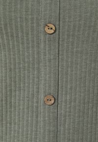 Grön ribbad tyg med två träknappar framtill. Texturen är mjuk och slät, med vertikal ribbning genomgående.