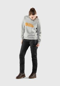Grå sweatshirt med orange logga, svarta byxor med cargofickor och bruna stövlar med orange detaljer, med en avslappnad passform och slitstarkt material.