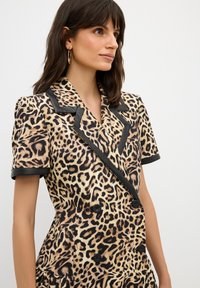 Blazer con stampa leopardo caratterizzato da un design doppiopetto, bordi neri, maniche corte e bottoni decorativi. Tessuto dalla consistenza liscia.