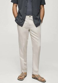 Lichtbeige broek gemaakt van gladde stof, recht model, gecombineerd met een donker shirt met korte mouwen en bruine sandaaltjes met bandjes.