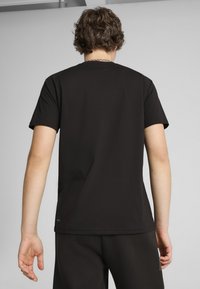 Czarny t-shirt z krótkim rękawem, wykonany z bawełny o gładkiej fakturze, z okrągłym dekoltem, z metką logo przy dolnym brzegu, pokazany z tyłu.