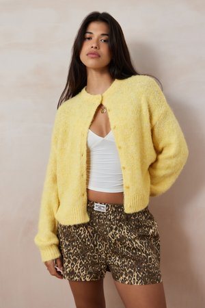 Cardigan amarillo de punto con cierre de botón, que presenta una textura suave y mangas anchas, combinado con pantalones cortos de estampado de leopardo.