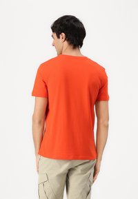 Orange kortærmet t-shirt i bomuld, med rund hals og lige snit, set bagfra mod en ensfarvet baggrund.