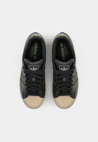 Melna ādas kedās ar zaļiem akcentiem, teksturētu purngalu un šņorēm. Satur Adidas logo uz mēles un iekšzoles. Klasisks dizains ar trim svītrām.