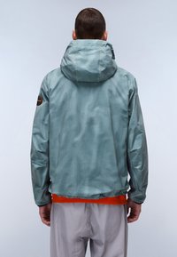 Lys blå jakke med rutemønster og hætte. Har et orange accent ved kanten og et mærke på venstre skulder. Struktureret stof.