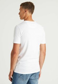 Biała bawełniana koszulka z okrągłym dekoltem i krótkimi rękawami, w połączeniu z jasnoniebieskimi dżinsami, widok z tyłu.