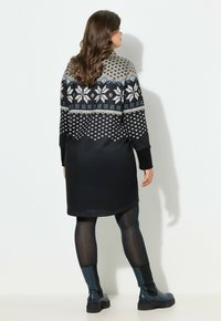 Strikket kjole med mønstret top i grå, hvid og blå; ensfarvet sort nederste del. Lange ærmer, afrundet kant, kombineret med mørke strømpebukser og ankelstøvler.