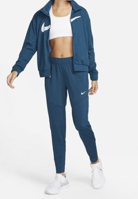 Marineblå Nike trackjakke med hvidt logo, kombineret med matchende joggingbukser og hvide sportssko, med afslappet pasform og elastisk taljebånd.