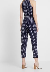 Granatowy kombinezon w kropki z dekoltem halter, dopasowanym w pasie i zwężonymi nogawkami. Posiada gładką fakturę i casualowy styl.