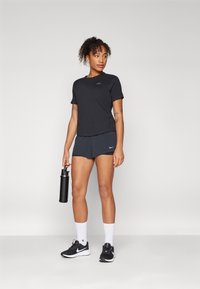 Svart trenings-T-skjorte og mørke grå shorts, med en liten logo. Sorte joggesko og hvite sokker. Holder en svart vannflaske.