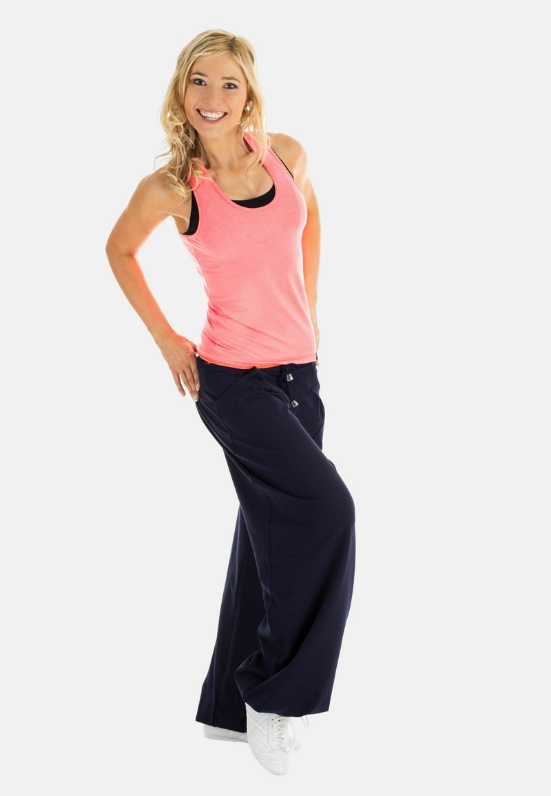 Rosa atletisk linne över en svart sport-bh, matchat med marinblå vida byxor. Vita träningsskor kompletterar outfiten.