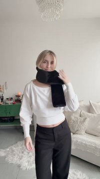 Svart skjerf pakket rundt halsen, laget av mykt stoff. Brukes med en hvit genser og svarte bukser. Rommets dekor inkluderer lyse farger og teksturer.