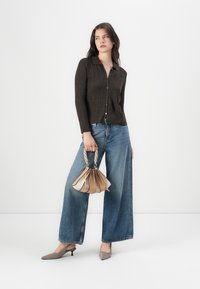 Brun randig knäppup topp, vida blå denimjeans, grå spetsiga klackar och en liten flerfärgad handväska med flätad handtag.