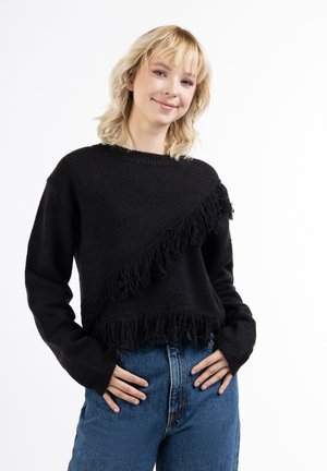 Czarny sweter z ukośnym wzorem frędzli wzdłuż dołu, z długimi rękawami i okrągłym dekoltem. Noszony z dżinsami o wysokim stanie.