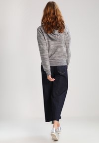 Felpa grigia con cappuccio e finitura testurizzata, abbinata a pantaloni larghi in denim scuro e scarpe argentate, vista da dietro.