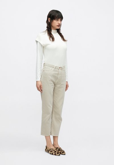 Λευκό τοπ με μακριά μανίκια και ψηλή λαιμόκοψη, συνδυασμένο με ανοιχτό μπεζ παντελόνια ευθείας γραμμής και παπούτσια slip-on με σχέδιο λεοπάρ.