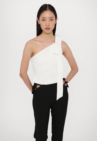 Asymmetrisch wit topje met een strikdetail op de linker schouder, gecombineerd met zwarte broek met zijstrikken. Soepele textuur, aansluitend ontwerp.