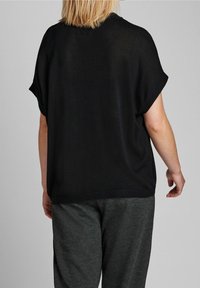 Schwarzes, oversized Oberteil mit kurzen Ärmeln, das einen lockeren Schnitt und eine weiche Textur aufweist. Kombiniert mit grauen Hosen, die für Komfort entworfen sind.