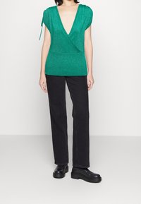 Groene, kortgebouwde top met V-hals en ribbeltextuur, in combinatie met zwarte, rechte broek en stevige zwarte laarzen.