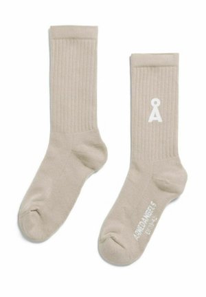 Beige ribgebreide enkelsokken met een wit "Å"-logo op de ene sok en de tekst "Amiø Angels" op de zool van de andere sok.