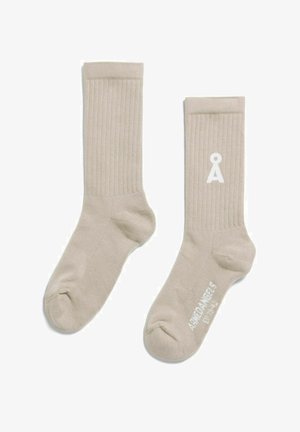 Chaussettes beige côtelées montant jusqu'à la cheville avec un logo blanc "Å" sur une chaussette et le texte "Amiø Angels" sur la semelle de l'autre chaussette.