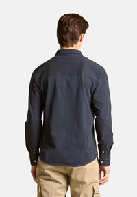 Camicia blu navy con maniche lunghe, polsini con bottoni e colletto classico. La vista posteriore mostra un orlo curvo e una cucitura dettagliata.