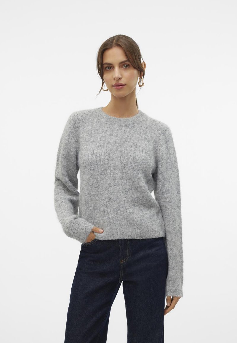 Grauer Strickpullover mit rundem Ausschnitt, langen Ärmeln und lockerer Passform. Weiche Textur, getragen über dunklen Jeans. Einfaches und klassisches Design.