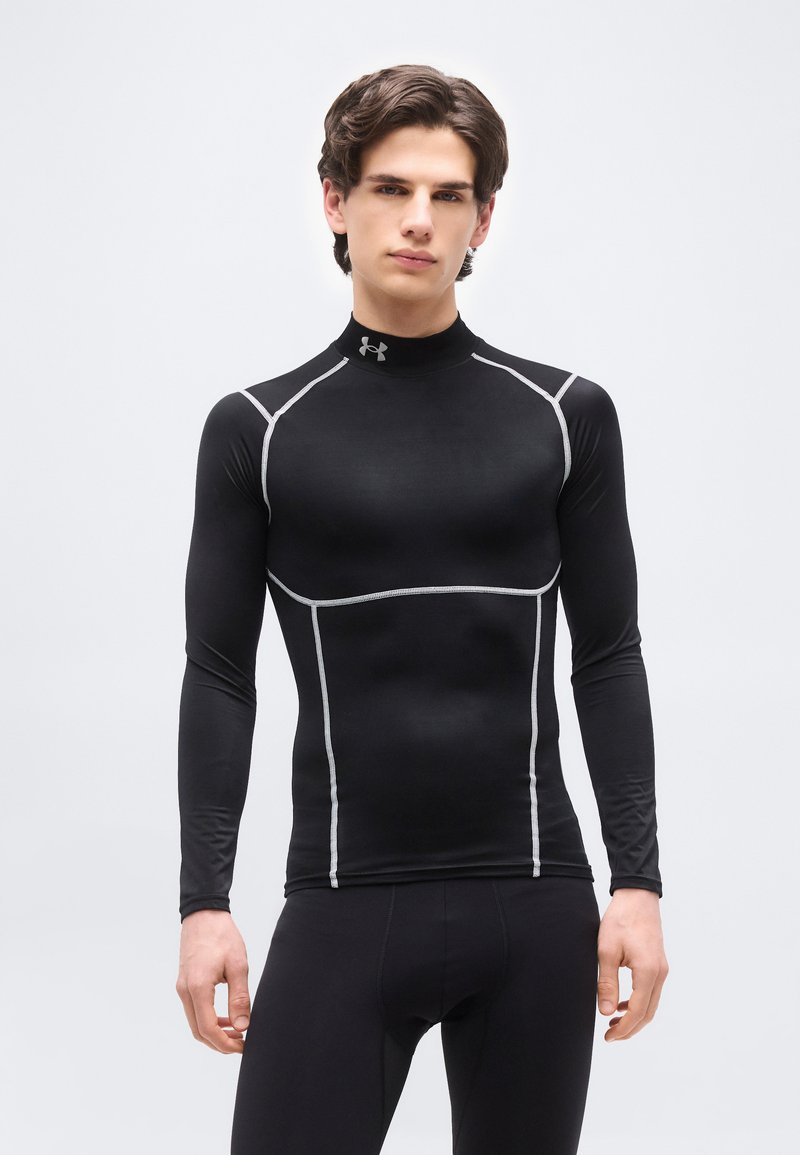 Νεαρός άνδρας που φοράει κοντομάνικο αθλητικό μαύρο τοπ με λευκή ραφή, όρθιος μπροστά σε απλό φωτεινό γκρι φόντο.