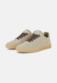 Beige suede sneakers with brown laces, perforated toe area, and a gum rubber sole. Simple design with minimal accents and stitching details.
