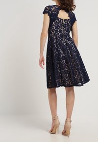 Námořnická modrá krajková šaty s krátkými rukávy, s předním zipem na zadní straně a zvlněnými detaily. Nosit s nahými lodičkami na vysokém podpatku.