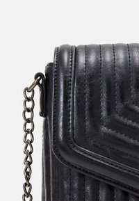 Bolso cruzado de cuero negro con un diseño acolchado, correa de cadena y un acabado texturizado. Presenta un cierre de solapa y un detalle de costura sutil.