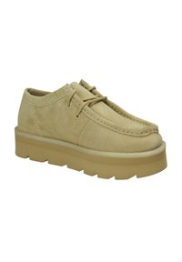 Scarpe in camoscio di un tenue color tan, con punta arrotondata, lacci minimal e una robusta suola in gomma di colore contrastante con bordi seghettati.