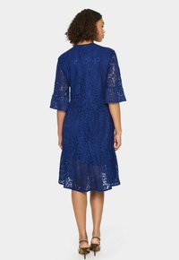 Rochie din dantelă de culoare albastră, cu mâneci până la cot și tiv evazat. Detalii cu model floral. Purtați cu tocuri înalte.