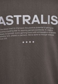 Grå t-shirt med stort hvidt tekst, der siger "ASTRALIS" og mindre tekst nedenfor. Glat stof uden synlige mønstre eller accenter.