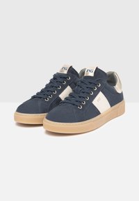 Baskets en daim bleu marine avec un détail de bande blanche, semelle beige et accents métalliques sur le talon. Conception à lacets avec une surface texturée.