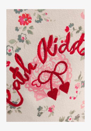 Text roșu brodat „Cath Kidston” cu două forme de inimă dedesubt, pe material crem cu modele mici florale roz, verzi și gri.