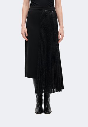 Jupe midi noire avec un côté en tissu lisse et l'autre côté plissé avec des sequins brillants, associée à des bottes noires.