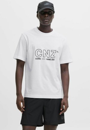 Hvid bomulds t-shirt med sort grafisk tekst "CNZ" og "CORE NINE ZER." Kombineret med sorte shorts, mod en neutral baggrund.