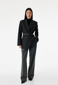 Grijze geruite blazer met een riem, gecombineerd met hooggewelfde grijze broeken. Beide stukken hebben een gestructureerd ontwerp en een textuurstof.