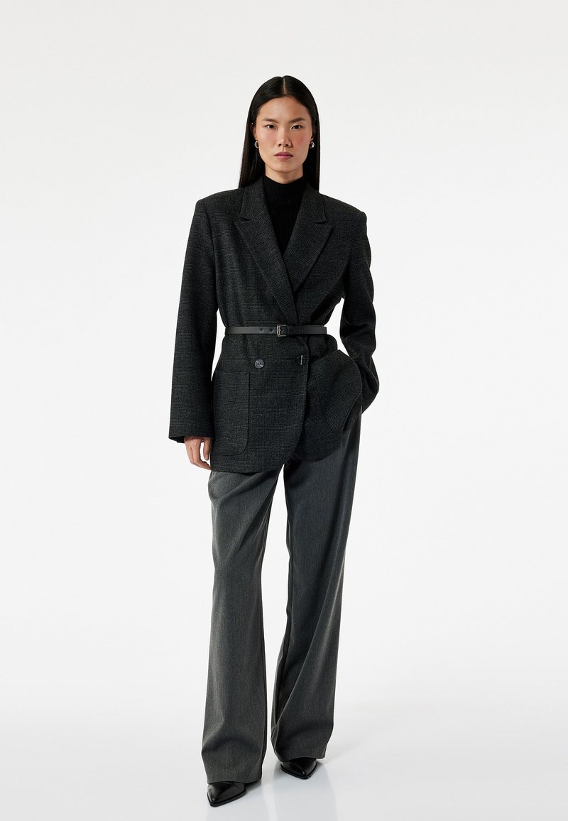 Grijze geruite blazer met een riem, gecombineerd met hooggewelfde grijze broeken. Beide stukken hebben een gestructureerd ontwerp en een textuurstof.