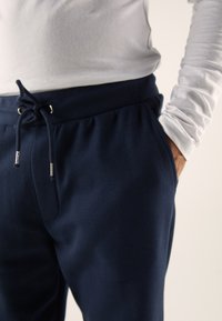 Laivastonsiniset joggers-housut, joissa on joustava vyötärönauha, kiristysnauha ja sivutaskut, valmistettu pehmeästä, teksturoidusta kankaasta.