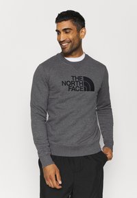 Felpa grigia realizzata in tessuto morbido, con un grande logo nero "The North Face" sul davanti, dotata di polsini e orlo a coste.