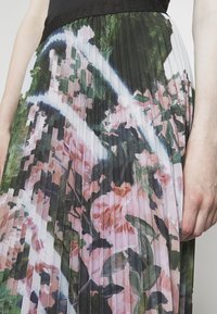 Gros plan sur une jupe plissée à imprimé floral abstrait dans des tons de rose, vert et blanc, portée avec une ceinture et un haut noirs.