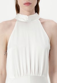Biely top na halterneck s textúrovaným povrchom, s gathered pásom a hladkým saténovým golierom. Jednoduchý, minimalistický dizajn.