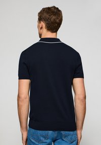 Marinblå polo tröja med klassisk krage, korta ärmar och vit kontrastsöm vid kragen och axeln. Texturerad stickad tyg.