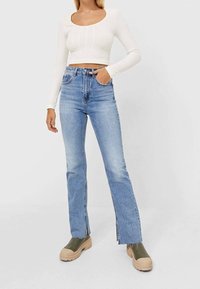 Biała, prążkowana, długosleeve crop top w połączeniu z jasnoniebieskimi, wysokim stanem dzwonami oraz masywnymi oliwkowymi platformami.