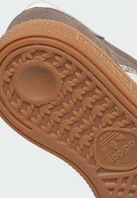 Nahaufnahme der Adidas-Schuhsohle mit strukturiertem, gumfarbenem Gummiprofil, das Trefoil-Logos und ein kreisförmiges Griffmuster zeigt.